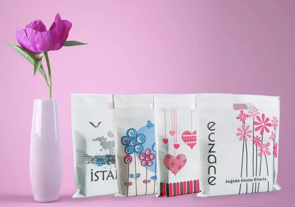 Pembe arka planda, solda tek bir pembe çiçekli vazo ve sağda eczane temalı baskılı, sıralı ultrasonik nonwoven kumaşlı bez torbalar yer almakta. Torbalar, seri üretim, dayanıklı ve çevre dostu.
